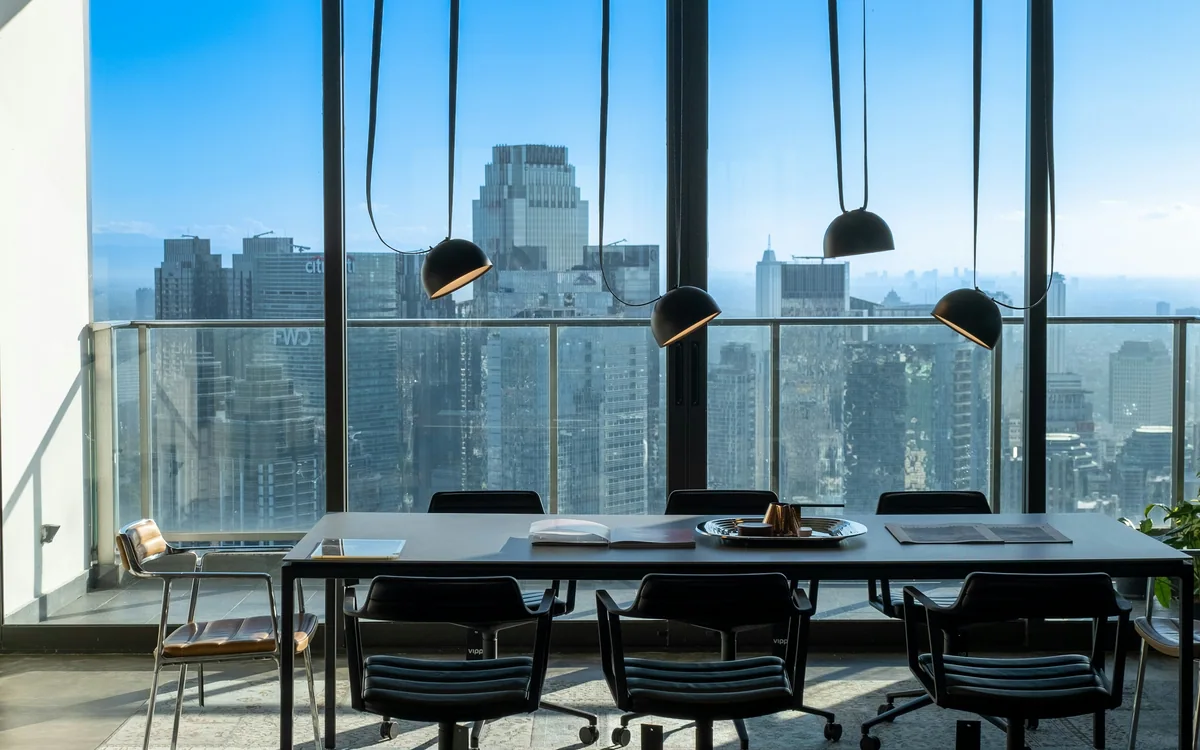 Mesa de reuniones junto a ventanales con vista a edificios urbanos.