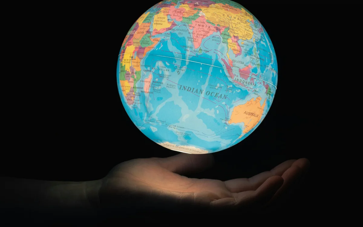 Globo terráqueo sostenido en una mano sobre un fondo oscuro.